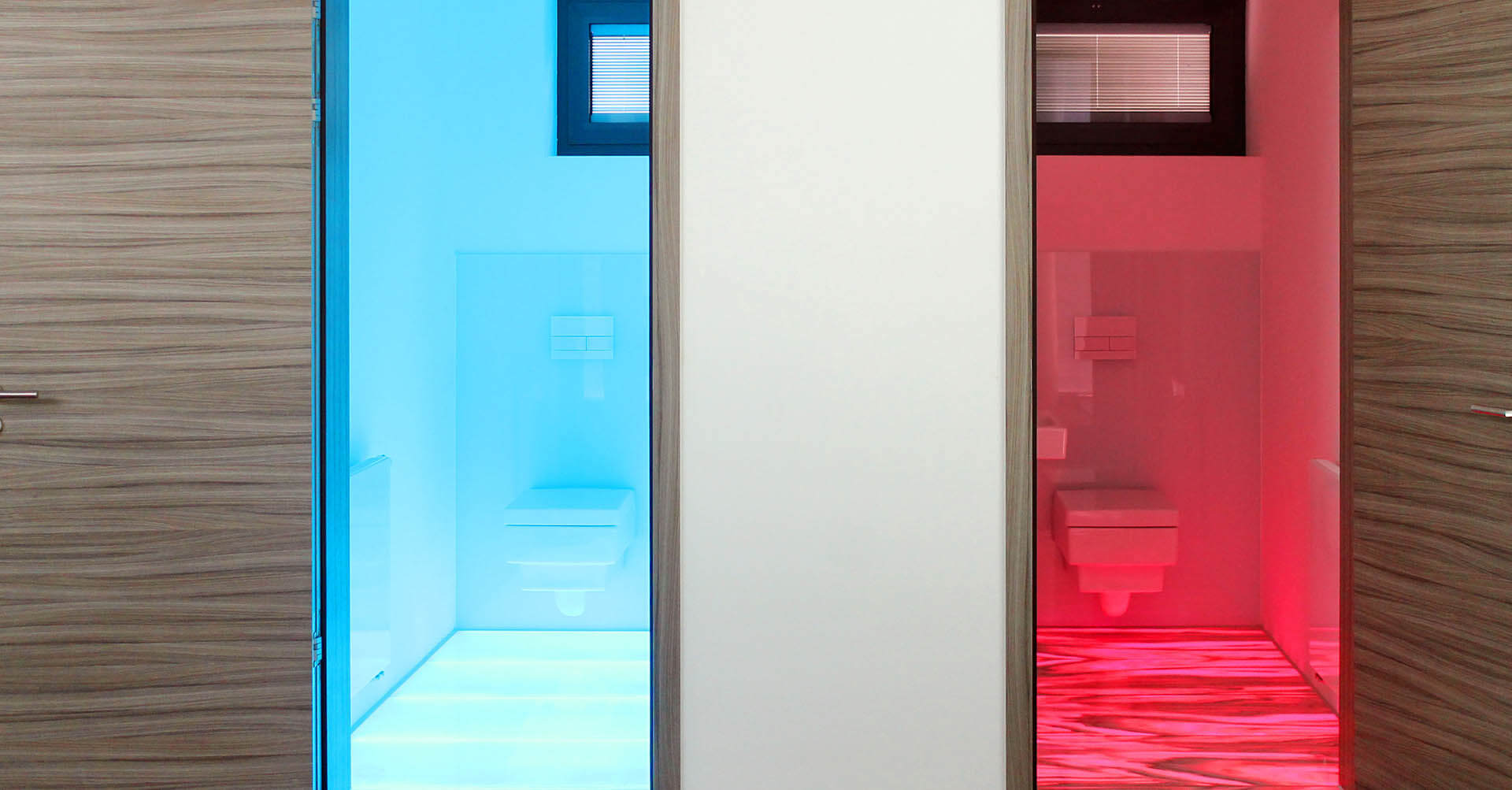 Zwei Toiletten mit LED-Bodenbeleuchtung: links blau beleuchteter Glas-Boden, rechts rot hinterleuchteter Marmor-Boden.