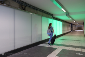 Das grüne Licht von LED-Paneelen folgt einer Passantin am Bahnhof Miltenberg.