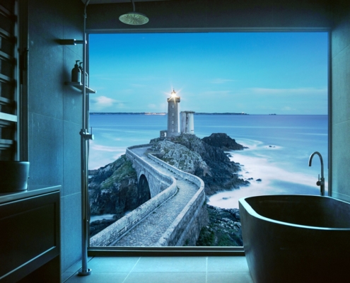 Graues Badezimmer, das von einer beleuchteten Duschrückwand beleuchtet wird. Das künstliche Fenster zeigt den Leuchtturm Petit Minou am Eingang zur Bucht von Brest (Rade de Brest) in der Gemeinde Plouzané in der Bretagne