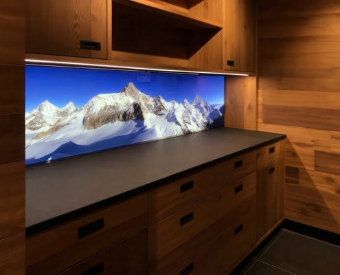 LED-beleuchtete Küchenrückwand aus Glas mit Motiv (schneebedeckte Berge) in einer modernen Küche aus Echtholz. Eine LED-Unterbauleuchte sorgt für noch mehr Licht.