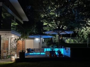 Hellblaue LED-Panels als Outdoor-Beleuchtung für eine Garten-Lounge neben einem Pool.