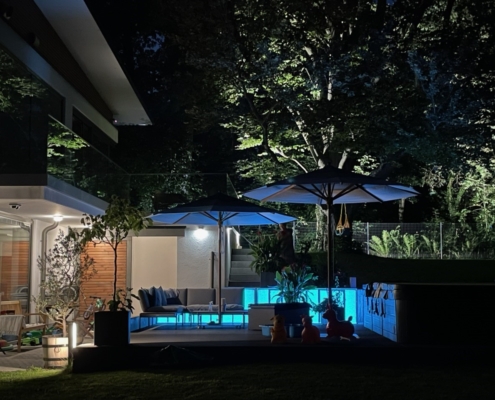 Hellblaue LED-Panels als Outdoor-Beleuchtung für eine Garten-Lounge neben einem Pool.
