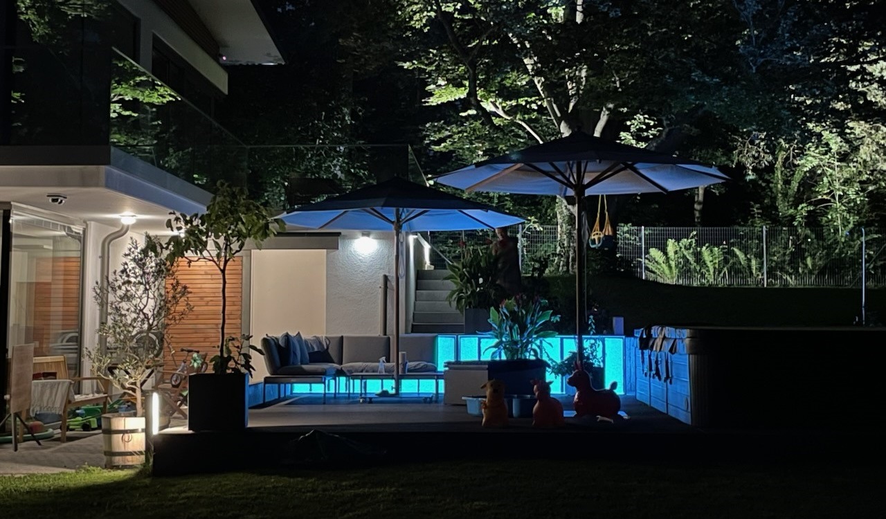 Hellblaue LED-Panels als Outdoor-Beleuchtung für eine Garten-Lounge neben einem Pool. Die Terrassenbeleuchtung ist wetterfest.