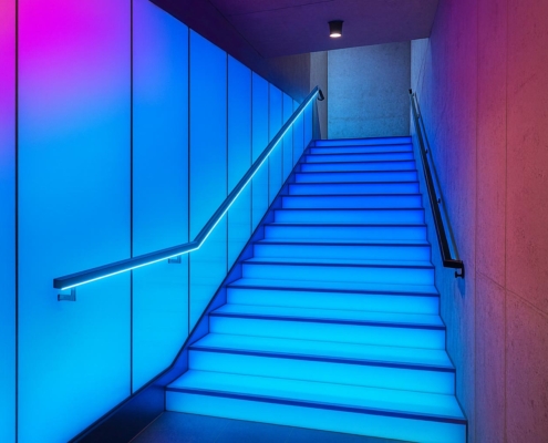 LED-Treppe mit blau leuchtenden Stufen und Setzstufen. Außerdem sind unter einem Handlauf LED-Stripes angebracht.